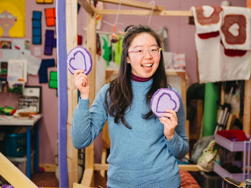 Woman holding up tufted coasters and smiling